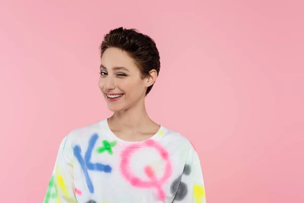 Mulher morena alegre na moda t-shirt piscando na câmera isolada em rosa — Fotografia de Stock