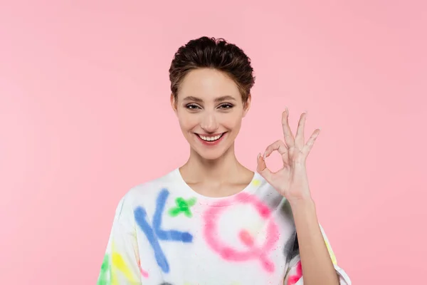 Positive woman with short hair showing ok gesture and smiling at camera isolated on pink — Stockfoto