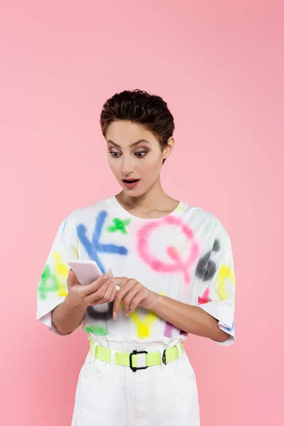 Astonished brunette woman with open mouth using mobile phone isolated on pink — Stock Photo