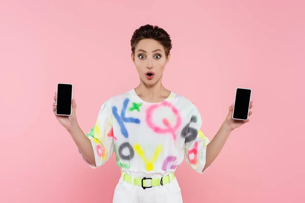 Überraschte brünette Frau zeigt Smartphones mit leerem Bildschirm isoliert auf rosa — Stockfoto