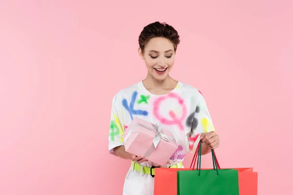 Pleased brunette woman with gift box and shopping bags isolated on pink — Stock Photo