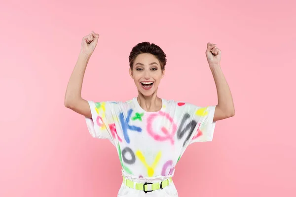 Excited young woman with short hair showing triumph gesture while looking at camera isolated on pink — Stockfoto