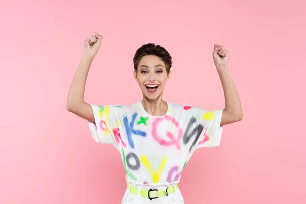 Excited young woman with short hair showing triumph gesture while looking at camera isolated on pink — стоковое фото