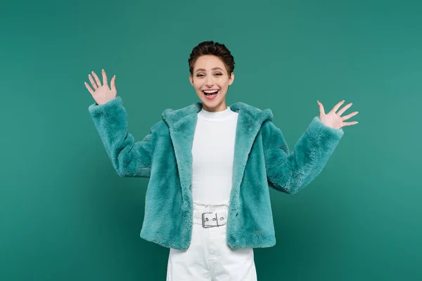 Excited brunette woman in faux fur jacket waving hands isolated on green — Stockfoto