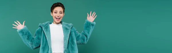 Excited woman in faux fur jacket waving hands while looking at camera isolated on green, banner — Foto stock