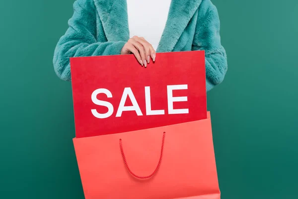 Vista recortada de la mujer en chaqueta de piel sintética con bolsa de compras rosa y tarjeta de crédito con letras venta aislado en verde - foto de stock