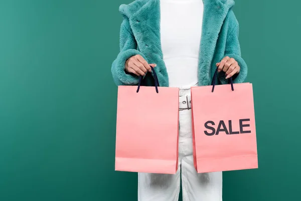 Vista ritagliata della donna in giacca di pelliccia sintetica che tiene in vendita borse della spesa isolate sul verde — Foto stock