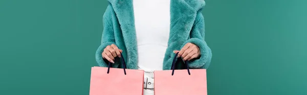 Cropped view of woman in trendy faux fur jacket holding pink shopping bags isolated on green, banner — Stockfoto