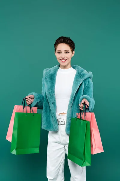 Femme heureuse et à la mode avec des sacs multicolores souriant à la caméra isolée sur vert — Photo de stock