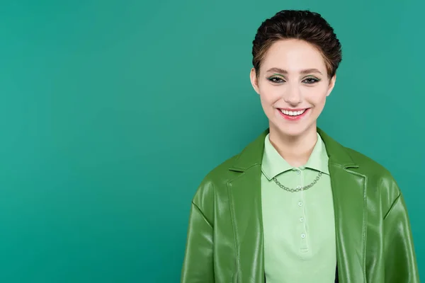 Cheerful brunette woman in stylish jacket looking at camera isolated on green — Stock Photo