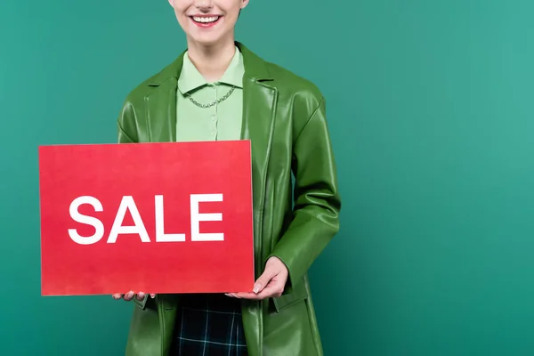 Vista recortada de la mujer en chaqueta elegante con tarjeta roja con letras venta aislado en verde - foto de stock