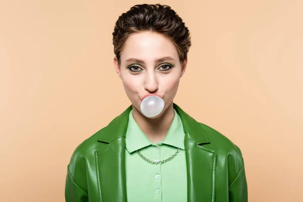 Trendy brunette woman blowing bubble gum while looking at camera isolated on beige — Stock Photo