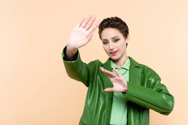 Brünette Frau in grüner Lederjacke gestikuliert, während sie isoliert auf beige posiert — Stockfoto