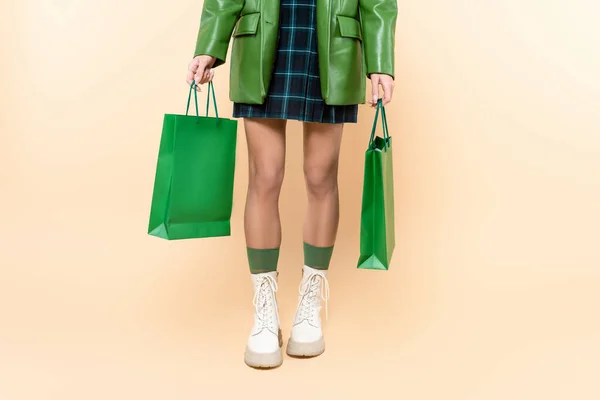 Cropped view of woman in plaid skirt and white lace-up boots holding shopping bags on beige — Stockfoto