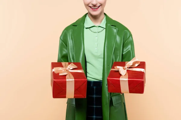 Обрізаний вид усміхненої жінки в зеленому піджаку, що тримає червоні подарункові коробки ізольовані на бежевому — стокове фото