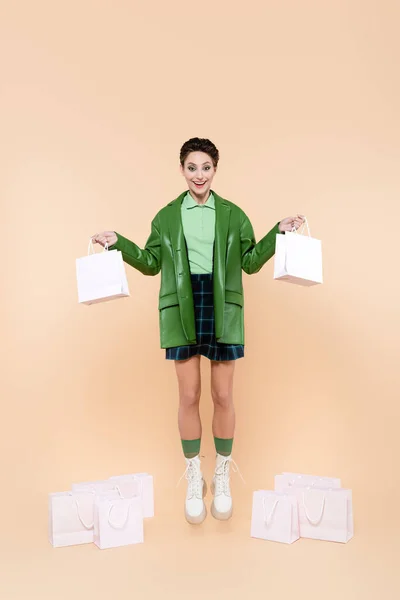Visão comprimento total da mulher animado em roupas da moda levitar com sacos de compras em bege — Fotografia de Stock