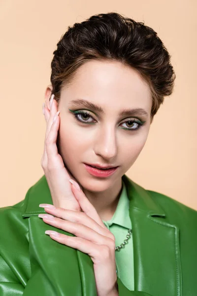 Portrait of young brunette woman with short hair looking at camera and touching face isolated on beige — Stockfoto