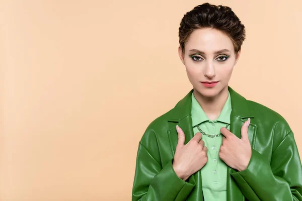 Junge Frau in grüner Lederjacke blickt in die Kamera, während sie isoliert auf Beige posiert — Stockfoto