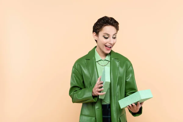 Amazed woman in green leather jacket looking in gift box isolated on beige — Stockfoto