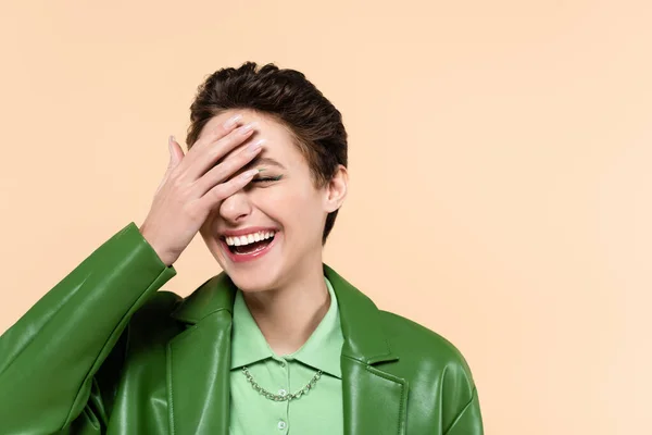 Young excited woman covering face with hand while laughing isolated on beige — стоковое фото