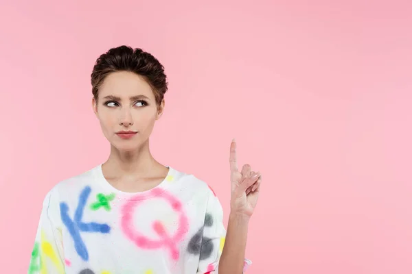 Serious brunette woman in stylish t-shirt pointing up with finger isolated on pink — Stock Photo