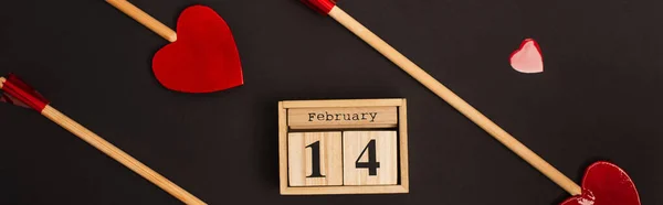 Top view of heart-shaped arrows near wooden cubes with 14 february lettering isolated on black, banner — Stock Photo