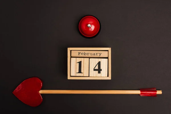 Top view of heart-shaped arrow near cubes with 14 february lettering and bell on black — Stockfoto