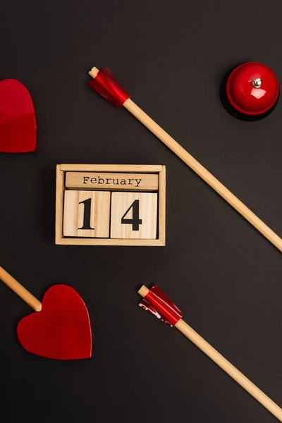 Vista superior de flechas en forma de corazón cerca de cubos con 14 letras de febrero y campana en negro — Stock Photo