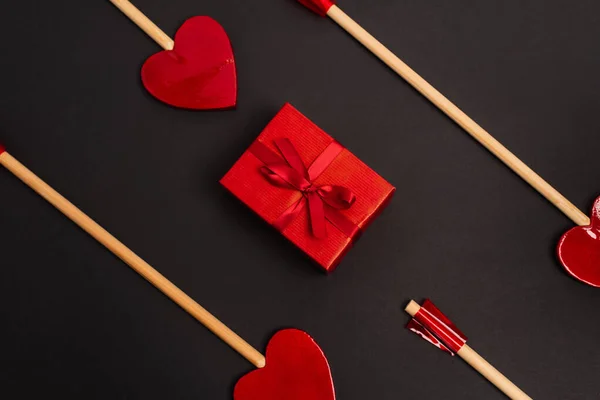 Top view of heart-shaped arrows near wrapped present on black — Stock Photo