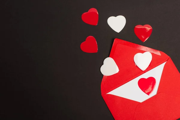 Top view of red envelope with love letter and paper cut hearts isolated on black — Fotografia de Stock