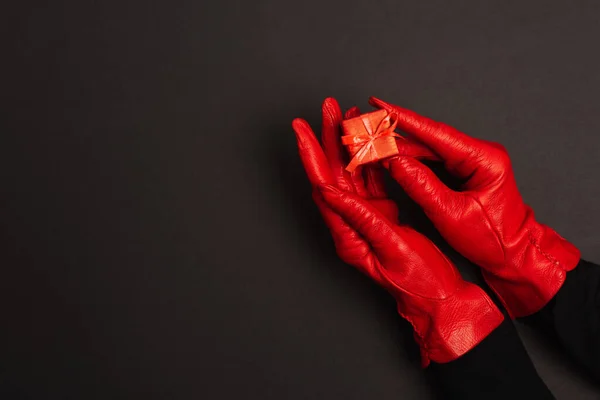 Обрезанный вид женщины в красных перчатках, держащей крошечную подарочную коробку на черном — стоковое фото