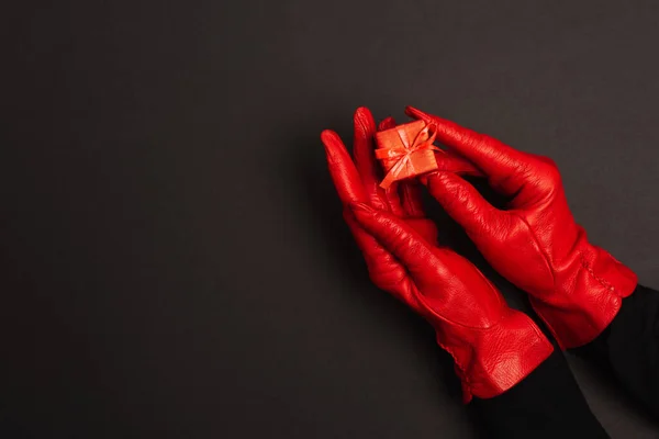 Cropped view of woman in red gloves holding tiny gift box on black — Stock Photo