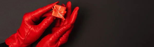 Vista recortada de la mujer en guantes rojos sosteniendo diminuta caja de regalo en negro, bandera - foto de stock