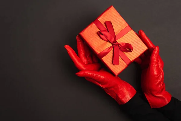 Cropped view of woman in red gloves holding wrapped present on black — Stock Photo