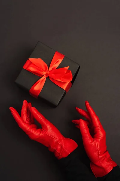 Vista recortada de la mujer en guantes rojos alcanzando regalo envuelto en negro - foto de stock