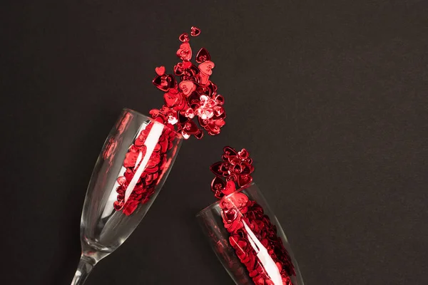 Top view of champagne glasses with red confetti hearts on black — Fotografia de Stock