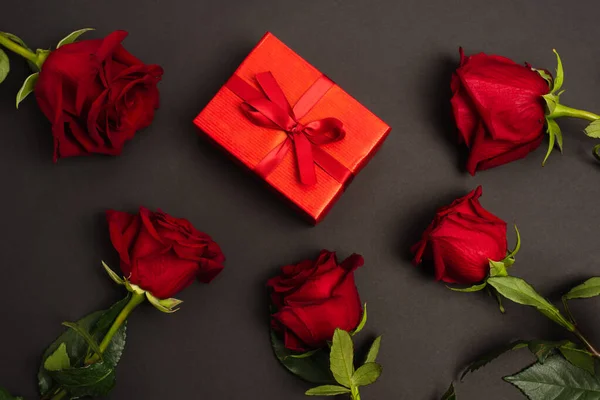 Disposición plana de rosas rojas cerca de la caja de regalo envuelta en negro - foto de stock