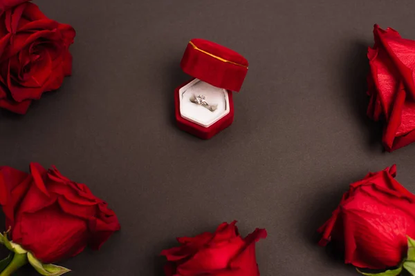 Vista superior da caixa de jóias com anel de diamante perto de rosas vermelhas em preto — Fotografia de Stock