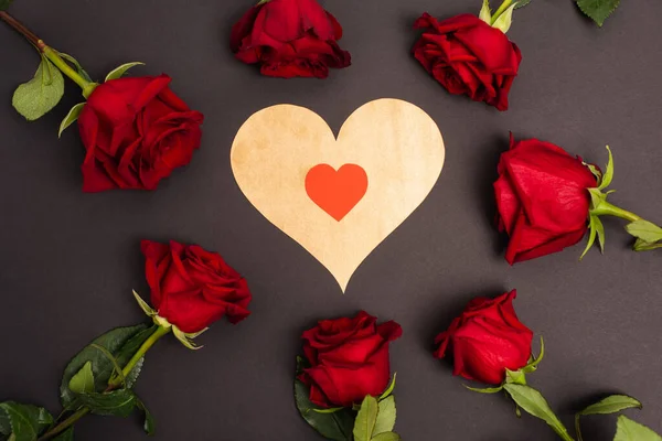 Flat lay of paper cut heart near red roses on black — Stockfoto