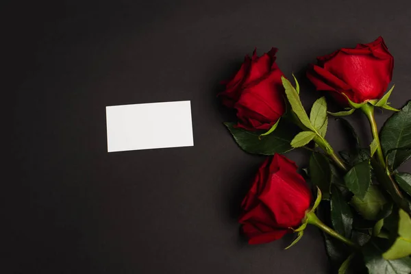 Top view of red roses near blank card on black — Stock Photo