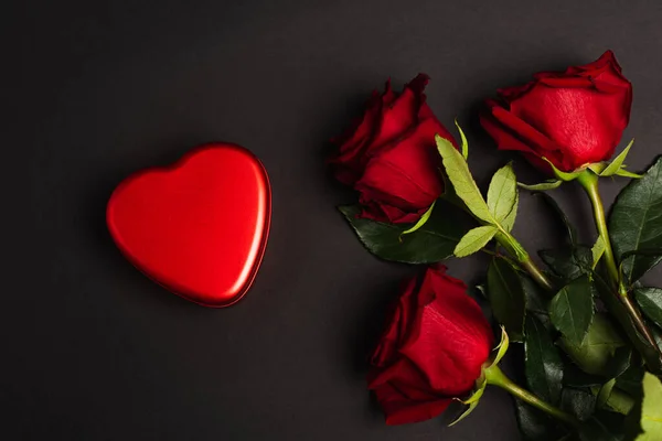 Top view of red roses near metallic heart-shaped box on black — Stock Photo