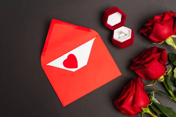 Верхний вид красных роз возле конверта и обручальное кольцо на черном — стоковое фото