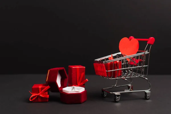 Boîte à bijoux avec bague en diamant près des cadeaux et petit panier sur noir — Photo de stock