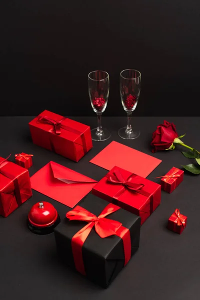 Wrapped presents and envelopes near metallic bell, rose and champagne glasses on black — Fotografia de Stock