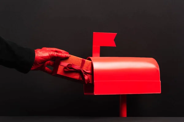 Partial view of person in red glove putting present in post box on black — Stock Photo