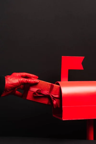 Cropped view of person in red glove putting wrapped present in post box isolated on black — Stock Photo