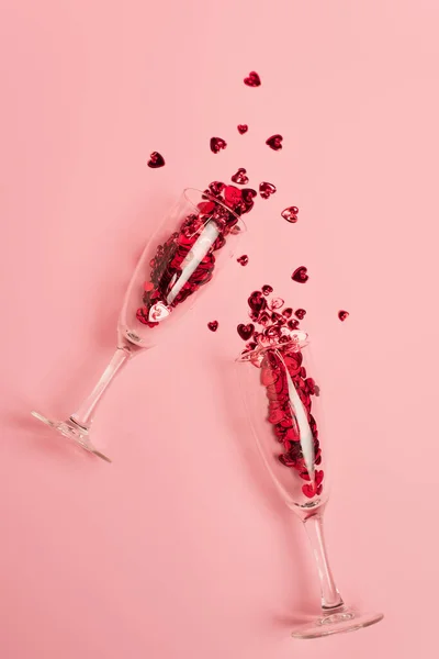 Top view of champagne glasses with red confetti hearts on pink — Stock Photo