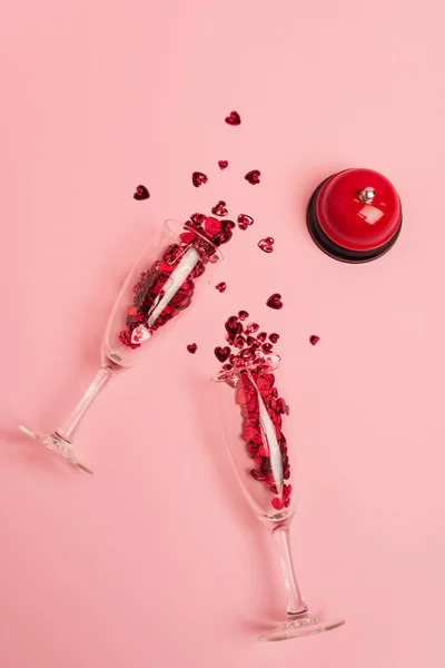 Vue de dessus des verres à champagne avec des cœurs de confettis près cloche métallique sur rose — Photo de stock