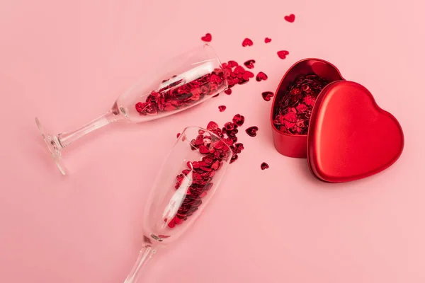 High angle view of champagne glasses with confetti hearts near metallic heart-shaped box on pink — Fotografia de Stock