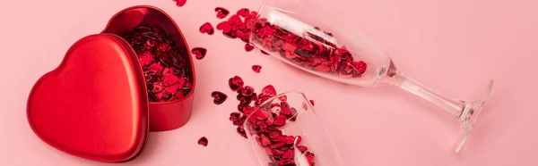 Vue grand angle des verres à champagne avec des coeurs de confettis près de boîte métallique en forme de coeur sur rose, bannière — Photo de stock